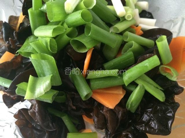 过凉的木耳和胡萝卜片沥干水分，放在一个容器里，放入葱段；