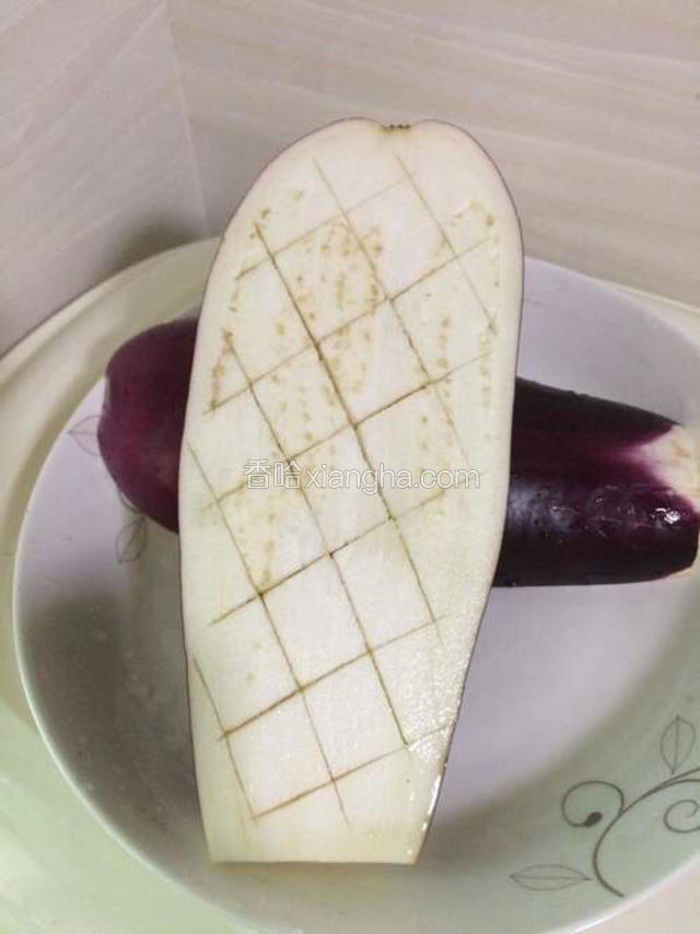 茄子对边切开两块，中间用刀划出菱形纹，为的是易熟，且容易入味。