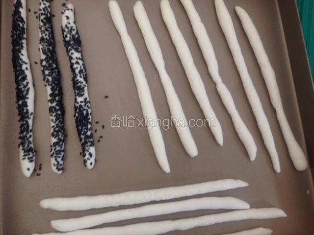 再对折捏紧收口，擀成长条状放入烤盘。表面喷水，放入芝麻里表面粘黑芝麻