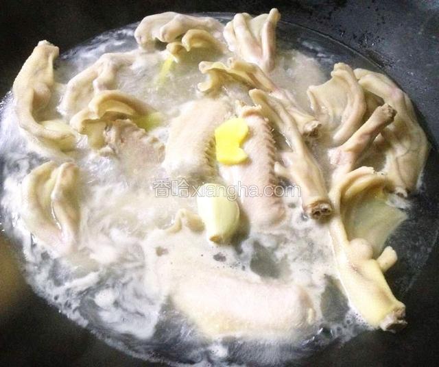 锅烧开水,放入几粒蒜头、几片姜,下鸭翅、鸭掌焯水.