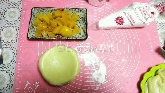 将黄桃切成块，打好的奶油装入裱花袋，取一块糯米粉擀揉圆沾熟糯米粉擀成片放在小碗上面