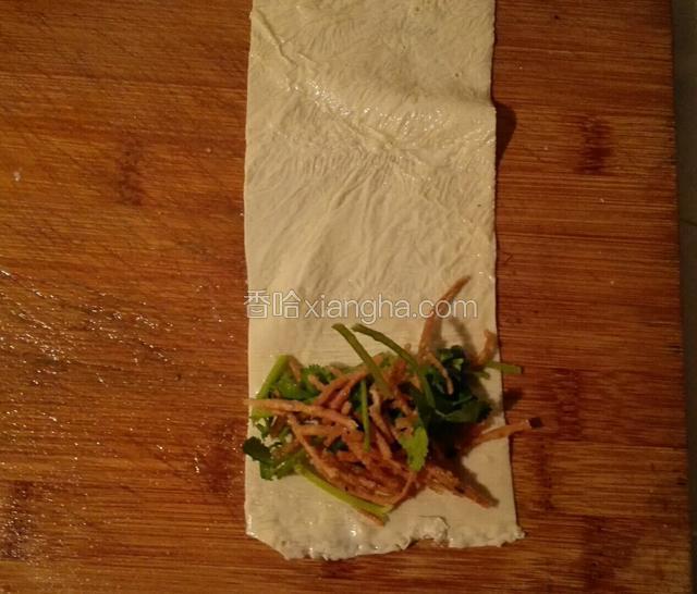 将调好的香菜和馓子卷入腐衣中。