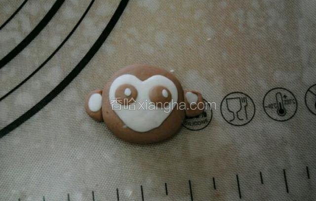 两个黄豆大小的面团压扁在白面团上做眼睛，剩下的两个可可面团压扁，把小的白面团压扁贴在上面做耳朵，再沾点水组合在猴头上，取两个芝麻大小的面团压在猴眼上做眼睛的着光点