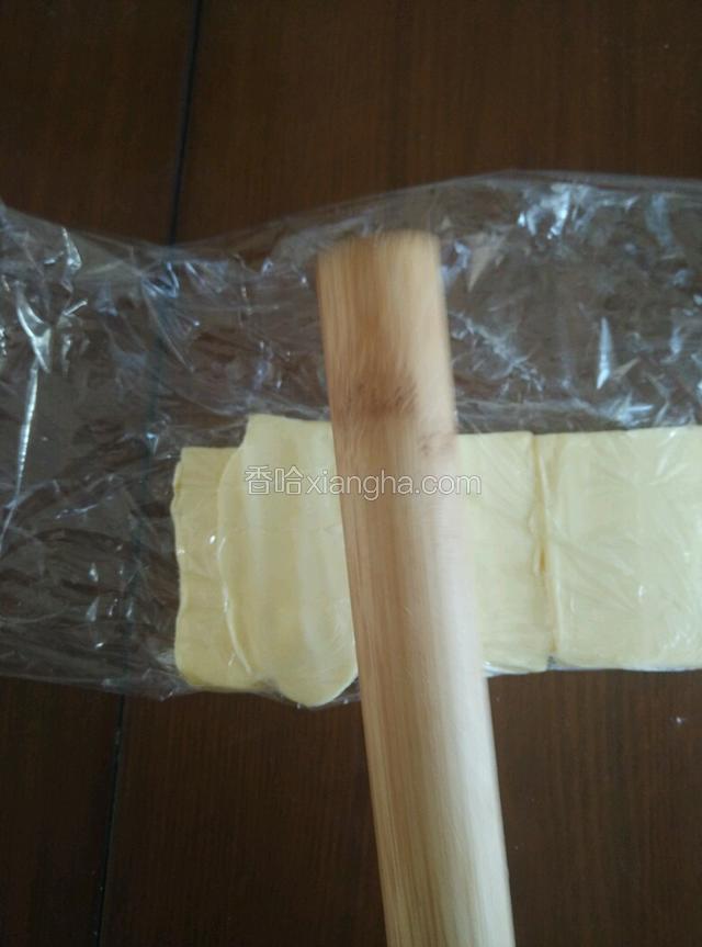 把65克黄油切成长方形，用保鲜膜包住，用擀面杖轻敲黄油，使之稍软。
