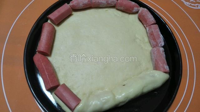 面团拿出擀圆放入十寸披萨盘，边上放入火腿肠，将火腿肠用饼边包裹住！