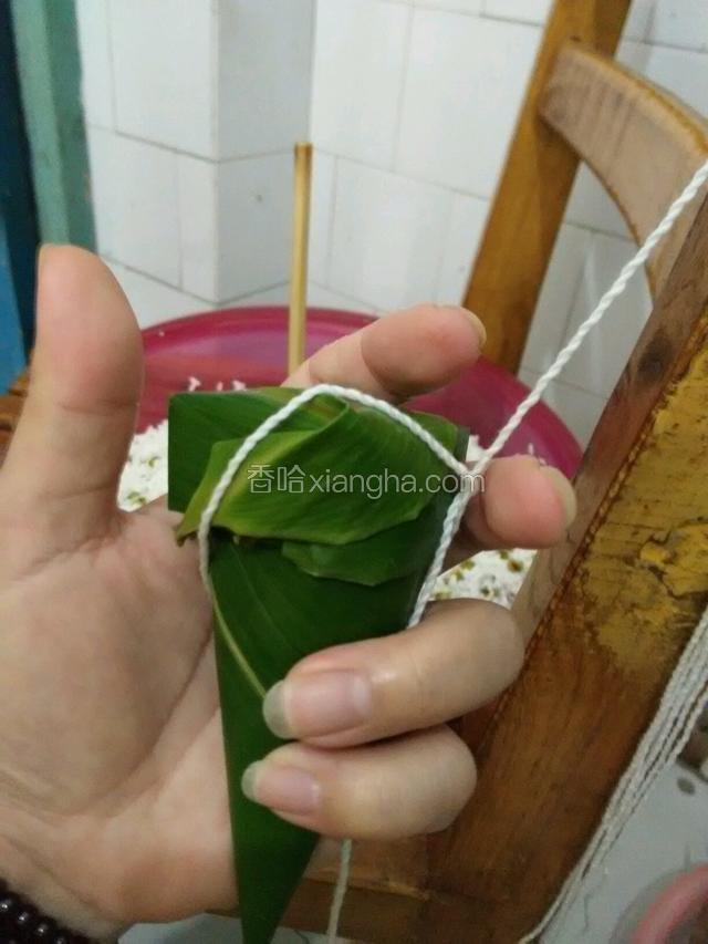 将绳子从粽子后面绕过打个节拉紧，再重复绕一次，打活节系紧