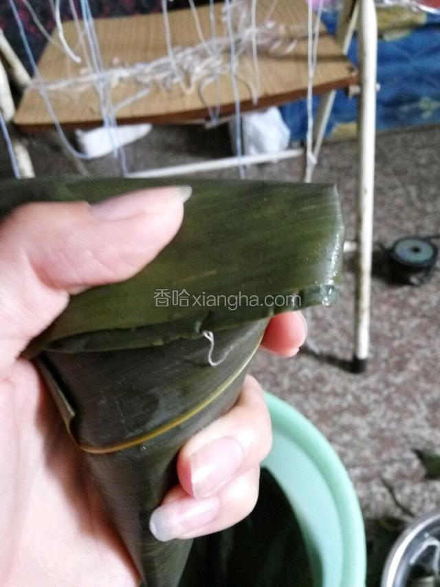 放满了糯米，后面的粽叶往前面盖，两边折下去，还剩一点粽叶尾巴往一边再折。最后用绳子绑紧。
