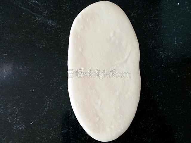 松弛好的面团用擀面丈从中间向上擀，再回到中间向下擀，成椭圆状。边缘所有气泡用手拍掉。