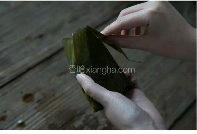 将长的粽叶推下来盖住米，包成三角形，多于的叶子贴合粽叶。