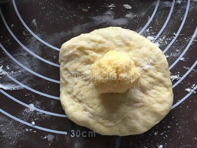 硅胶垫撒薄粉，取一个松弛好的面团，排气按扁，放入一份椰蓉馅儿。