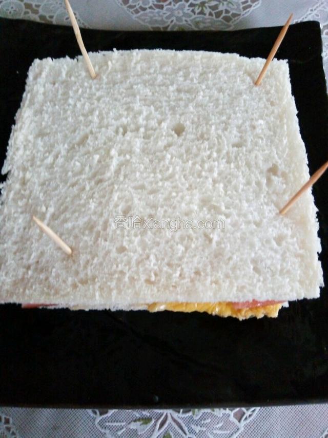 再把一片吐司抹上沙拉酱，盖在最上层，用四根牙签固定，一分为二就可以了。美味的三明治就可以享用了。