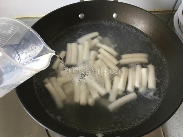 煮一大锅水大火煮开，沸腾时下入年糕条；转中小火煮至再次沸腾时加入少量冷水。