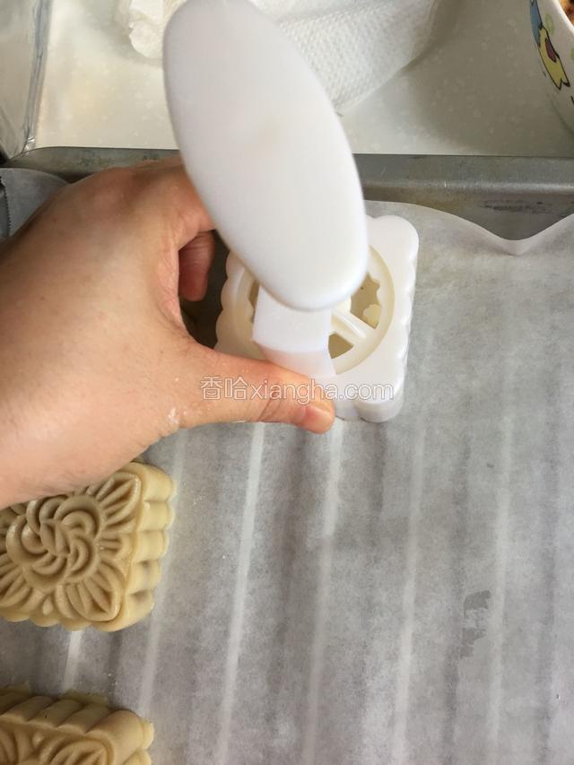 把模具放烤盘上，左手按住下面，右手用力按住上面往下压，注意不要太过于用力，以免把月饼挤出来
