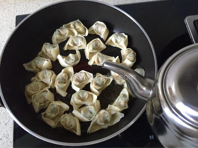 待水分焖干，馄饨也基本熟了，这个时候揭开锅盖，倒入适量油，手拿起锅柄将锅转动几次，使每一个馄饨均匀涂抹上油。