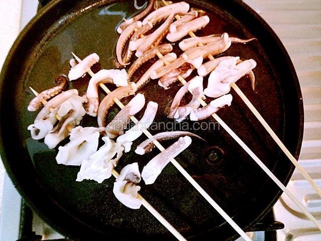 铁锅中烧油下入串好的鱿鱼须煎制