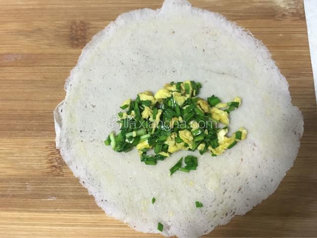取一张平铺在菜板上，一侧放入韭菜鸡蛋馅后卷，
