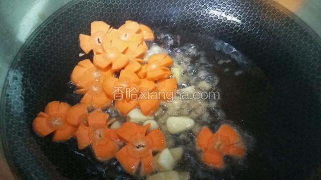 油温五成热倒葱姜蒜爆香，接着放胡萝卜花片翻炒。