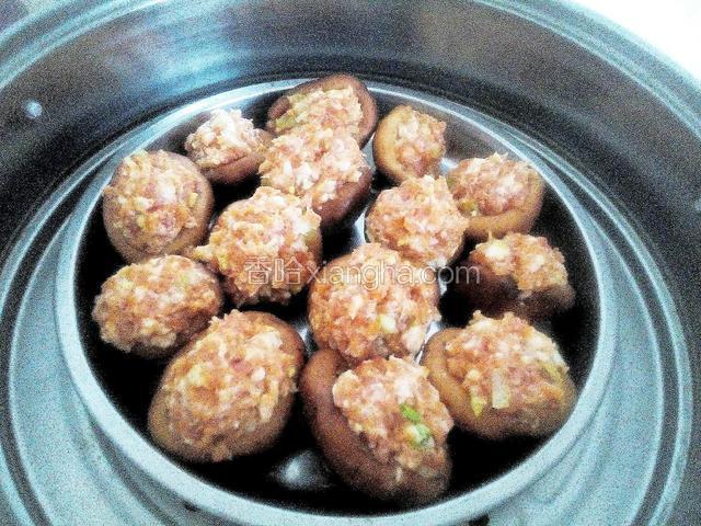 把拌匀的肉馅塞入香菇帽里，码在钢盆里，上蒸锅蒸熟，