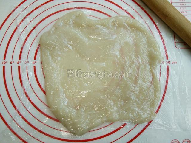 将糯米饼放擀面垫上，盖上保鲜膜，用擀面杖擀，糯米饼有弹性，慢慢擀