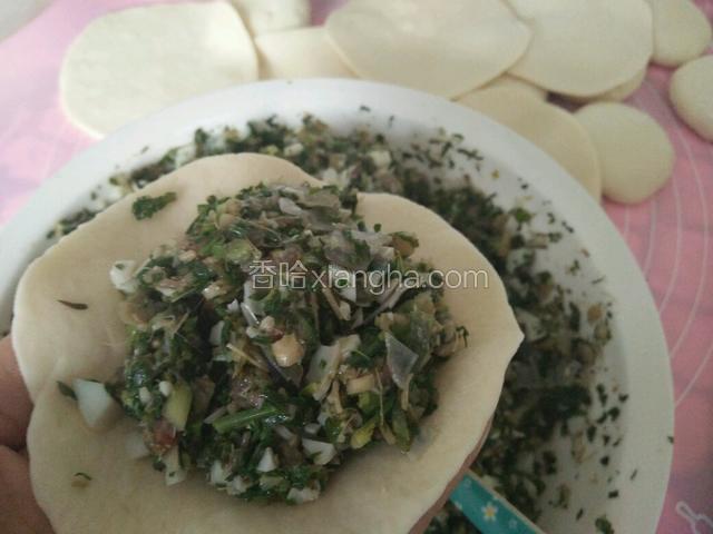 左手拿起包子皮，用掌心托住中间，五指分开拖住包子皮的边缘，挖起包子馅放入中间。