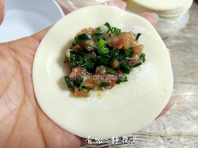 取一张饺子皮，放入适量肉馅，用右手食指沾一点点水在饺皮边缘抹一圈