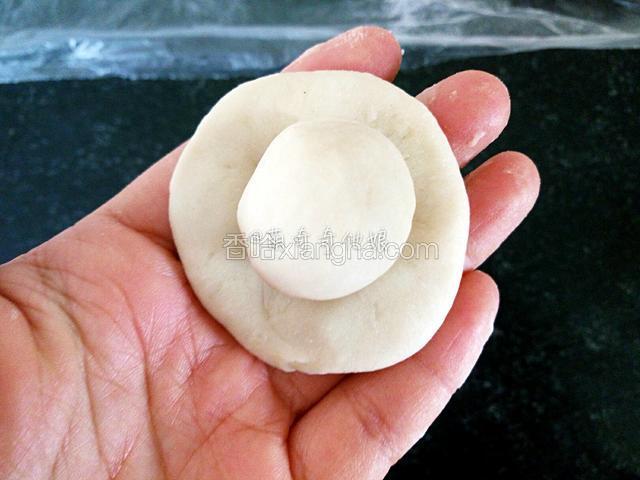 取一个松弛好的面团，放手心压扁，放入一颗油酥。
注意上面的油皮按顺序放好，每一次操作都从第一个开始。