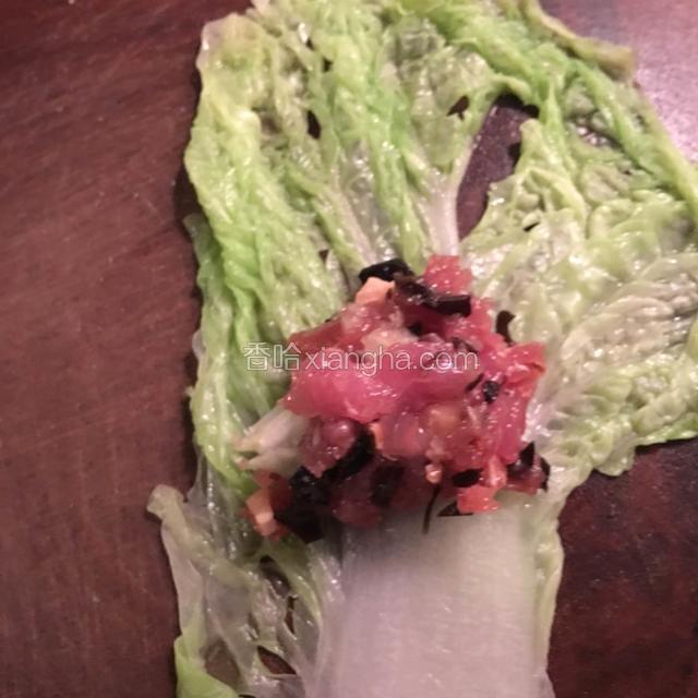 铺上一张白菜叶子，放上肉馅，从下往上卷起来，把菜梗包在里面。
