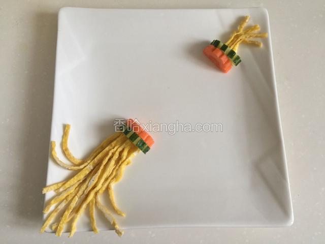 将鸡蛋饼切丝做灯笼的穗，胡萝卜和黄瓜切半圆，刻成齿轮状，在盘子上摆出灯笼的头和尾。