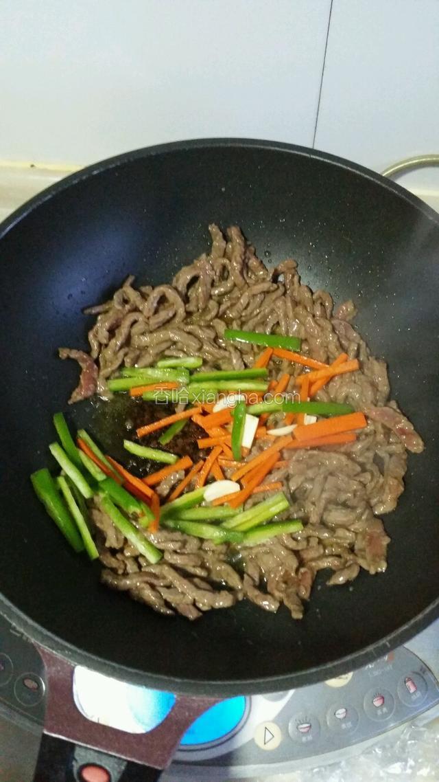 炒至牛肉变白时加入姜蒜，胡萝卜洋葱丝和青椒丝翻炒。
