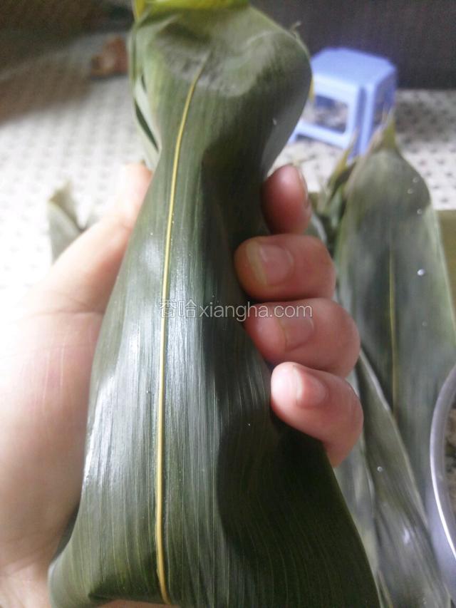 拿一片稍大点的粽叶用一半盖住上面，一半由下面绕上来用左手托住，上面的粽叶要完全覆住下面，两边捏紧。