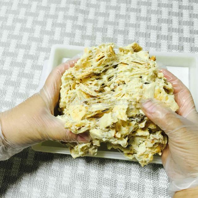 戴上提前准备的PVC一次性手套。
再用手拿起饼胚，往下翻拉几次，这样可以让牛扎糖更好的拉丝，粘住饼干和坚果仁。也会均匀些。这个过程部分饼干会碎是正常的，但不要用力捏碎饼干。
PS：家人帮拍的图，方便友友们看的清楚。这一步很重要，因为苏打饼太蓬松了，要这么操作糖才能均匀粘住其他材料。