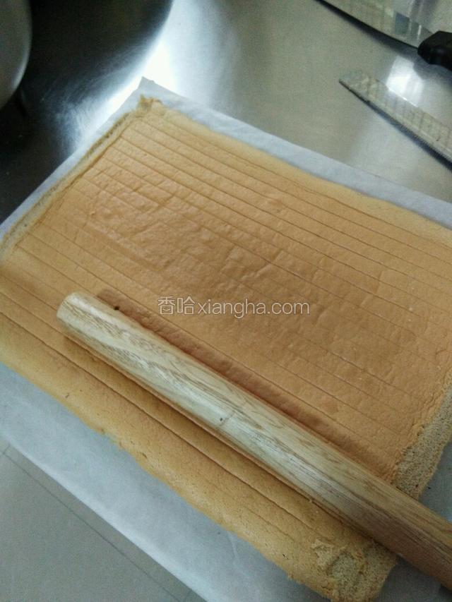待蛋糕冷却后，去纸，桌面铺上牛油纸，蛋糕放置其上，毛巾面朝下，擀面棍在约七八公分处压一道直痕；