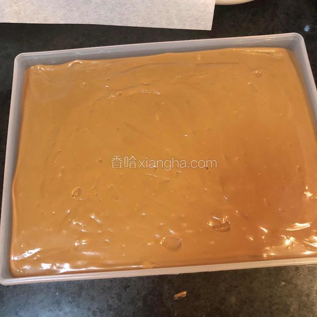 关火后糖浆在用刮刀在锅里翻拌一下，让糖体温度均匀冷却，等温度100度左右，将糖浆倒入到模具中，用刮刀将糖铺开，垫上一张油纸用压板轻轻压平，边角位置同样压平。