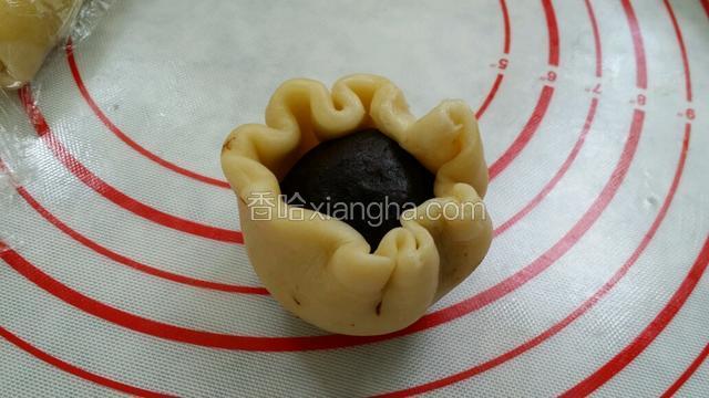 将静置好的面团搓圆，擀成饼皮，包上豆沙蛋黄球，收口朝下放入烤盘；