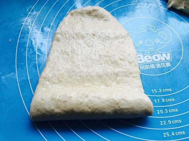 取一个面团擀成牛舌状，由下向上卷起。